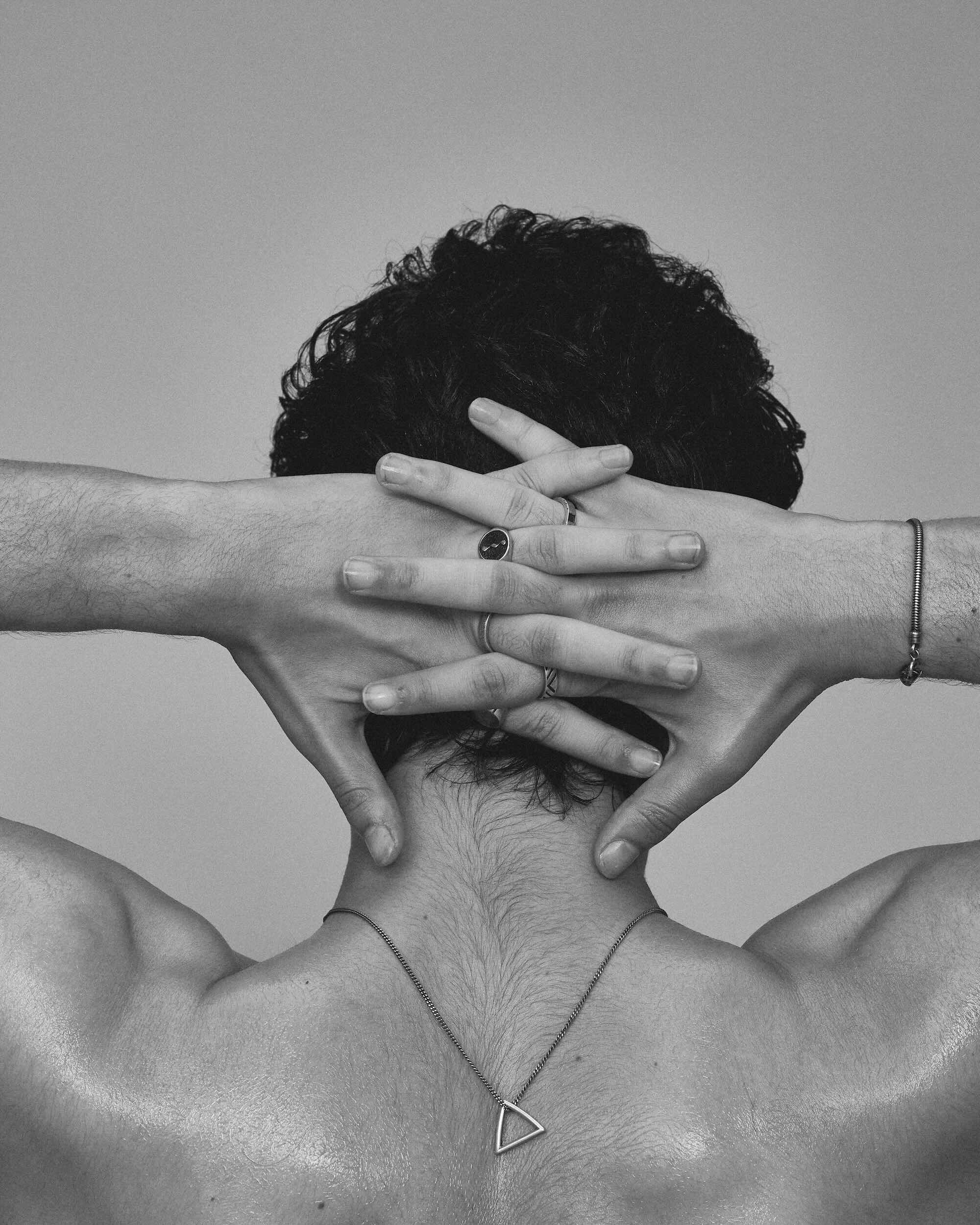 Black and white photo of a person with hands covering their face, wearing a necklace.