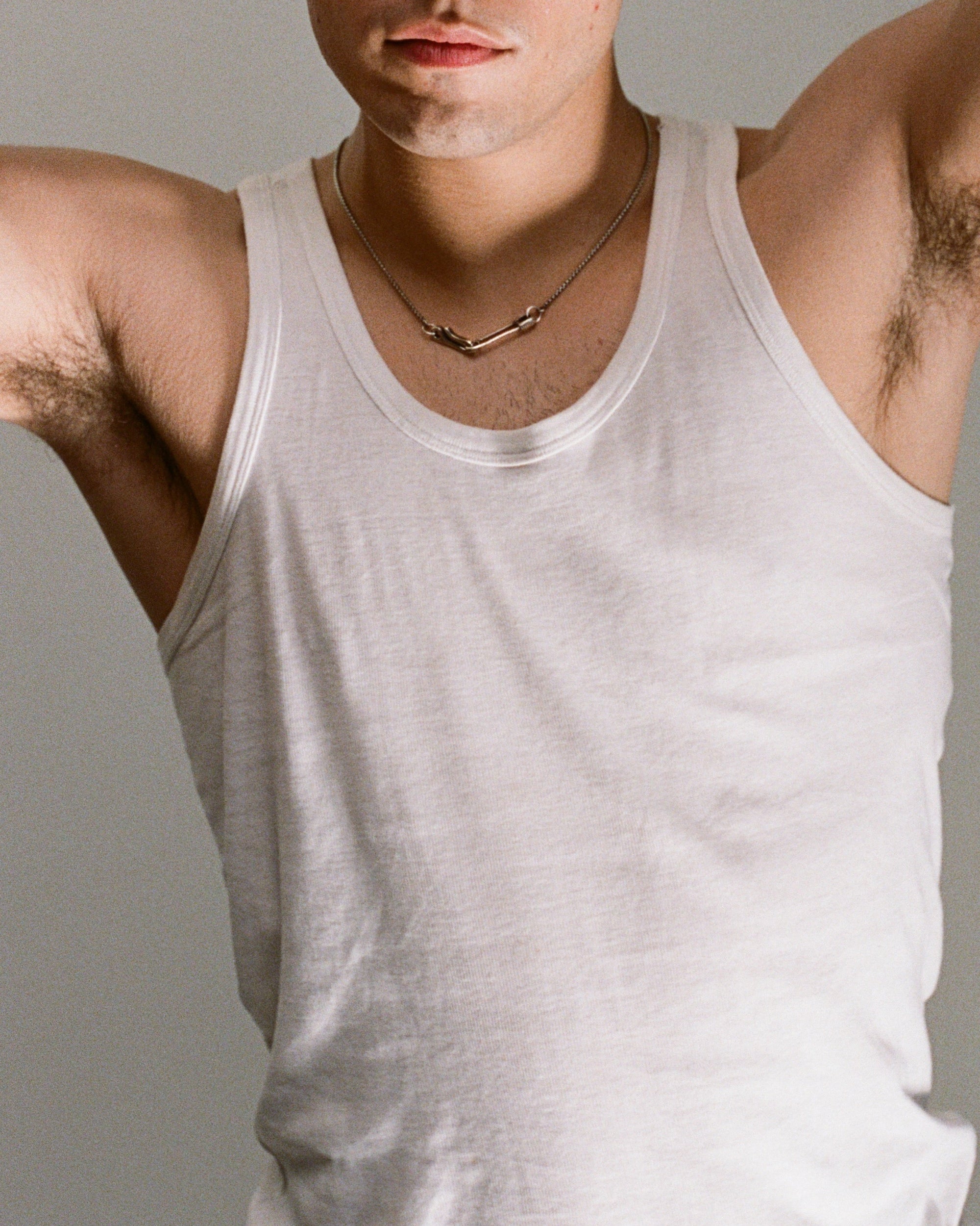 Man wearing a white tank top with a neutral background