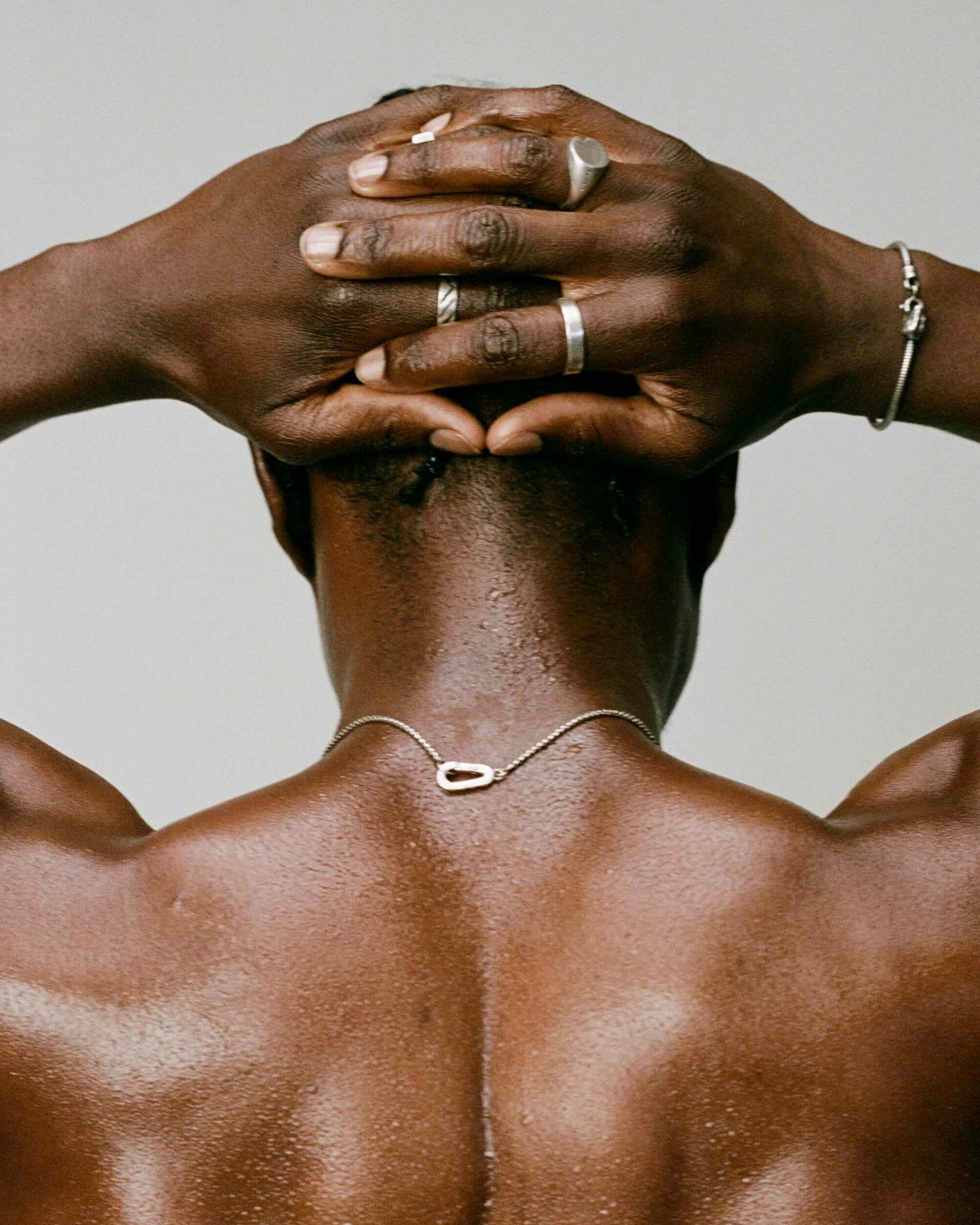 Man with muscular back and hands on head against a neutral background, 925 silver men's jewelry necklace