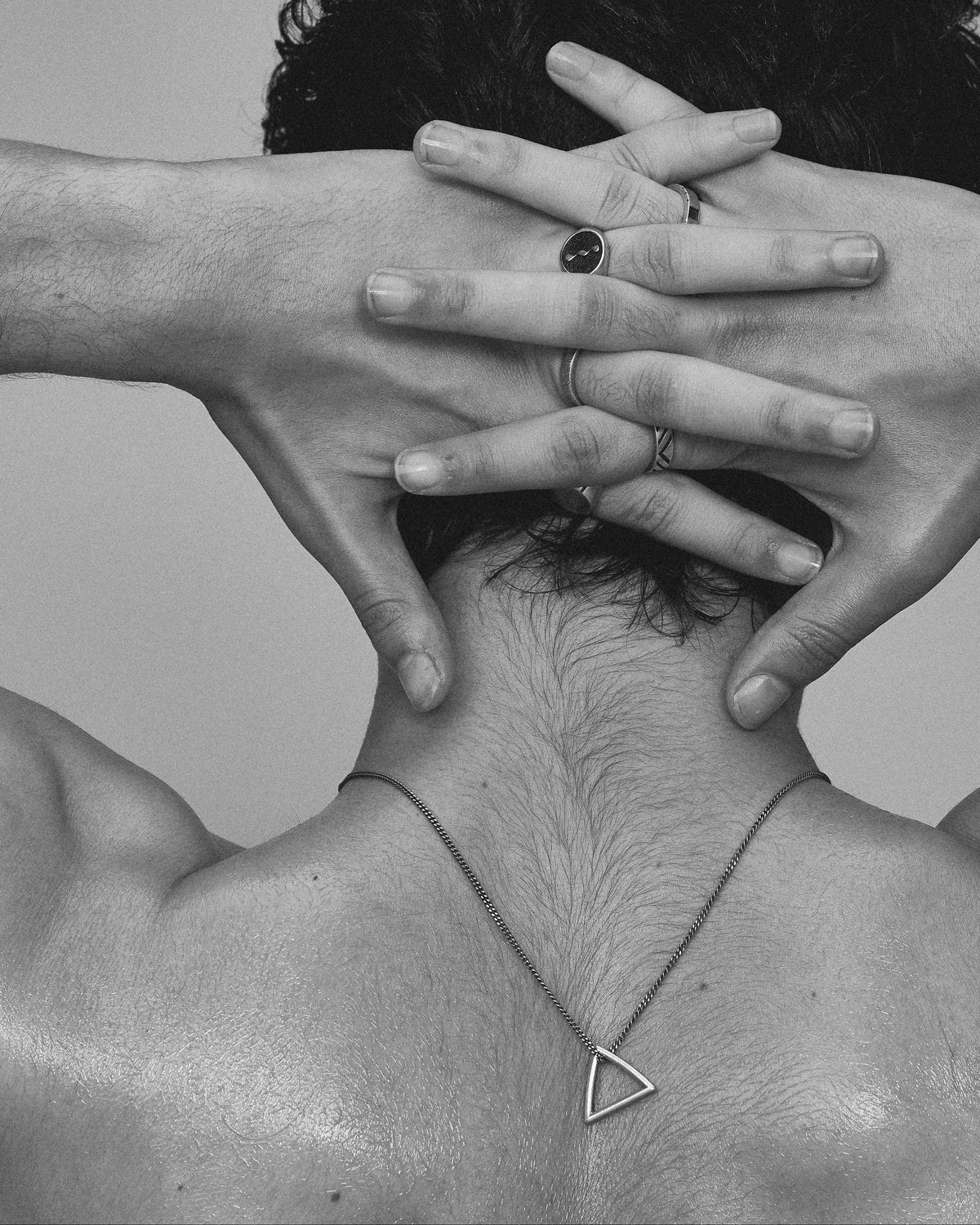Black and white photo of a person with hands covering their face, wearing a necklace.