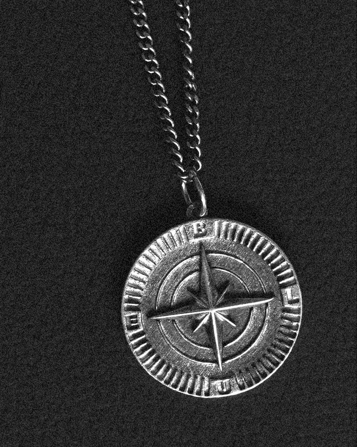 Two silver pendants on a chain against a black background