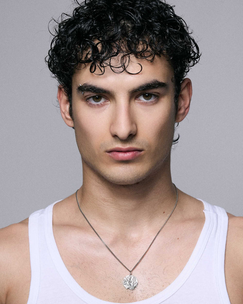 Man wearing a white tank top with a necklace against a gray background wearing 925 silver blue serpent jewelry