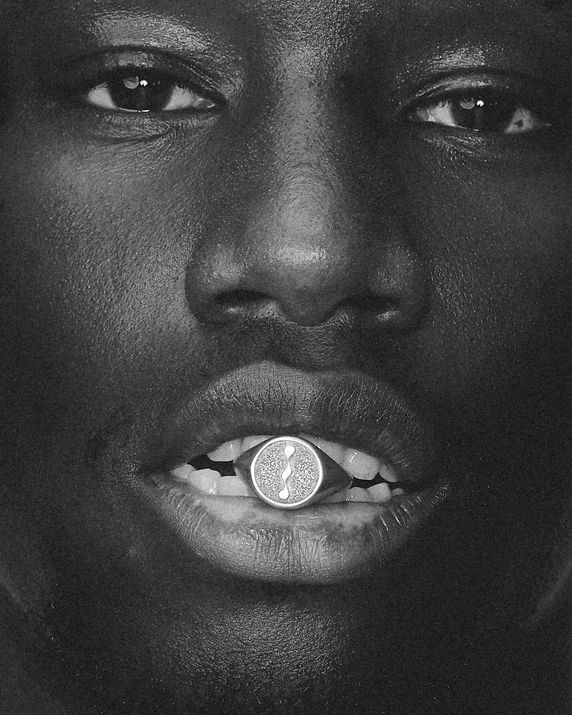 Close-up of a person's face with a portals blue serpent ring in their mouth, black and white photo