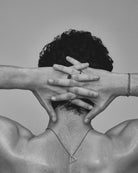 Black and white photo of a person with hands covering their face, wearing a necklace.