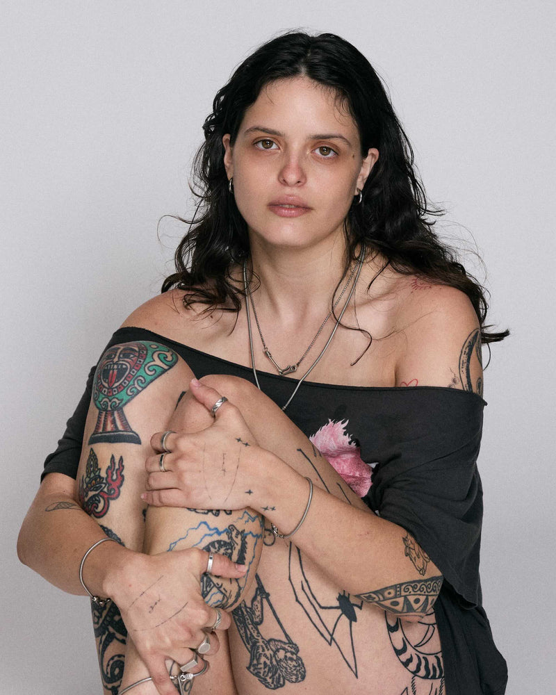 Woman with tattoos on her arms and chest against a plain background wearing 925 blue serpent rings and necklaces