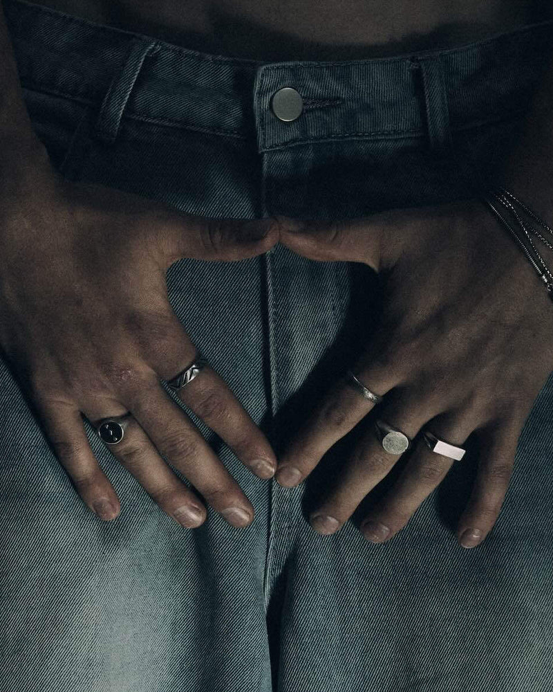 Person wearing a long denim skirt with hands on hips against a gray background wearing 925 silver mens rings / jewelry