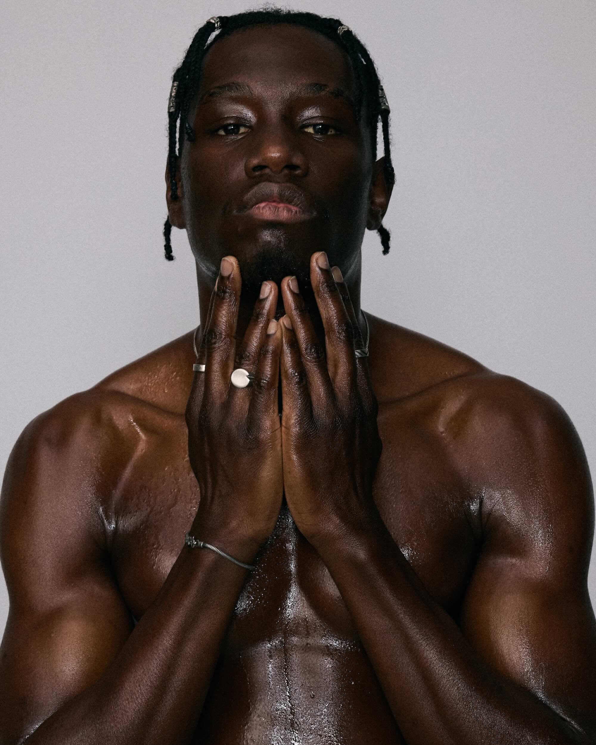 Man with braided hair holding his hands to his face against a plain background wearing forma ring 925 silver