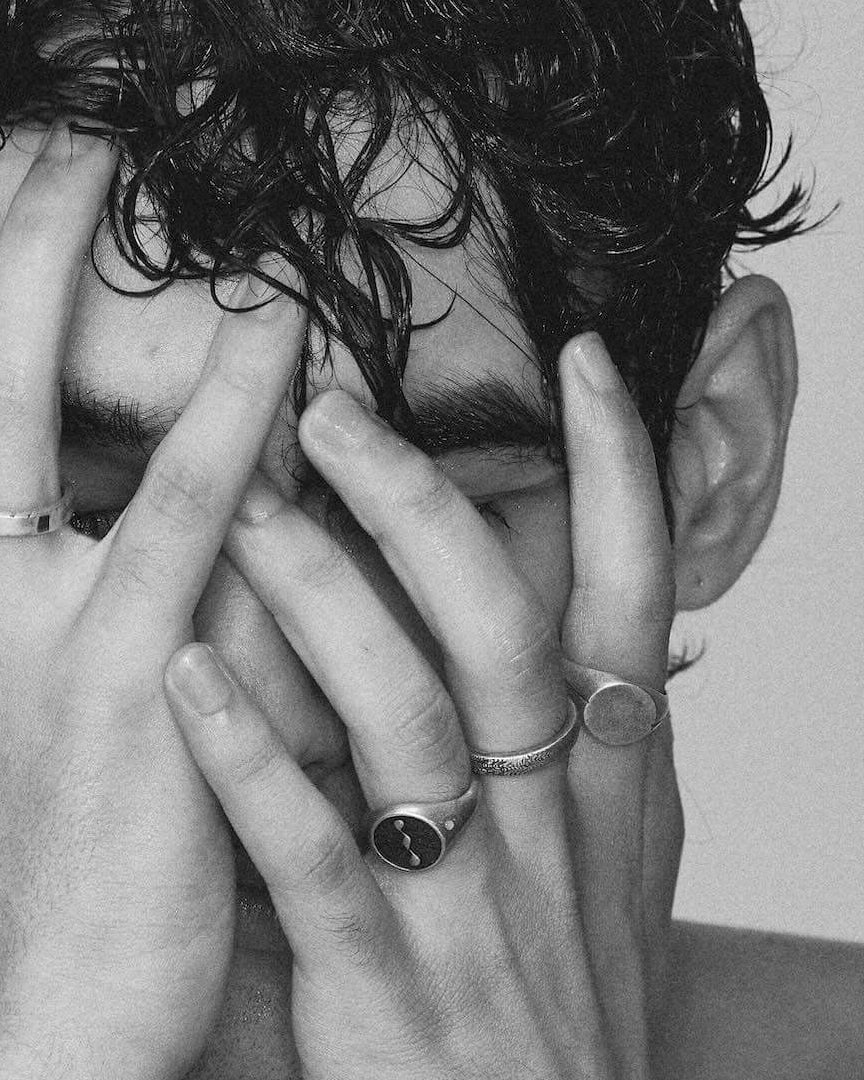 Black and white photo of a person with hands covering their face against a plain background wearing 925 silver jewelry